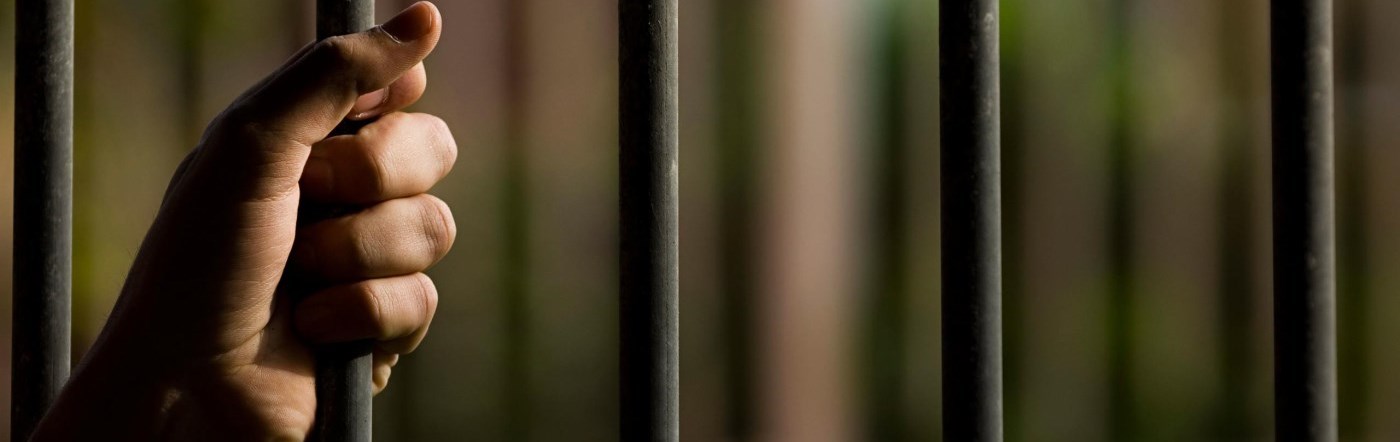 hands clasped on bars of prison cell