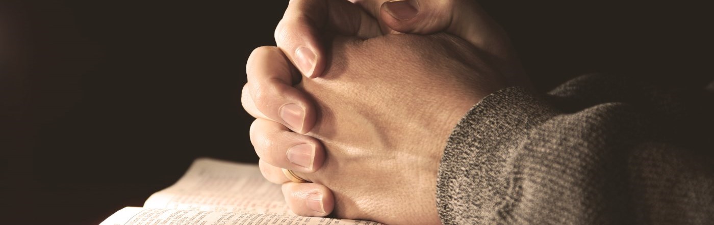Hands at prayer over a bible.